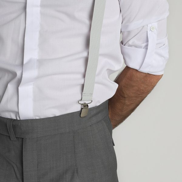 Detalle lateral de camisa Monk blanca con tiradores sobre pantalón gris